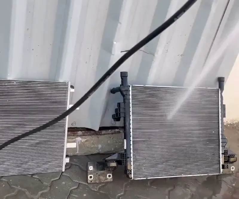 A radiator and an AC condenser taken out of a car, standing against a wall while they are washed with high-pressure water