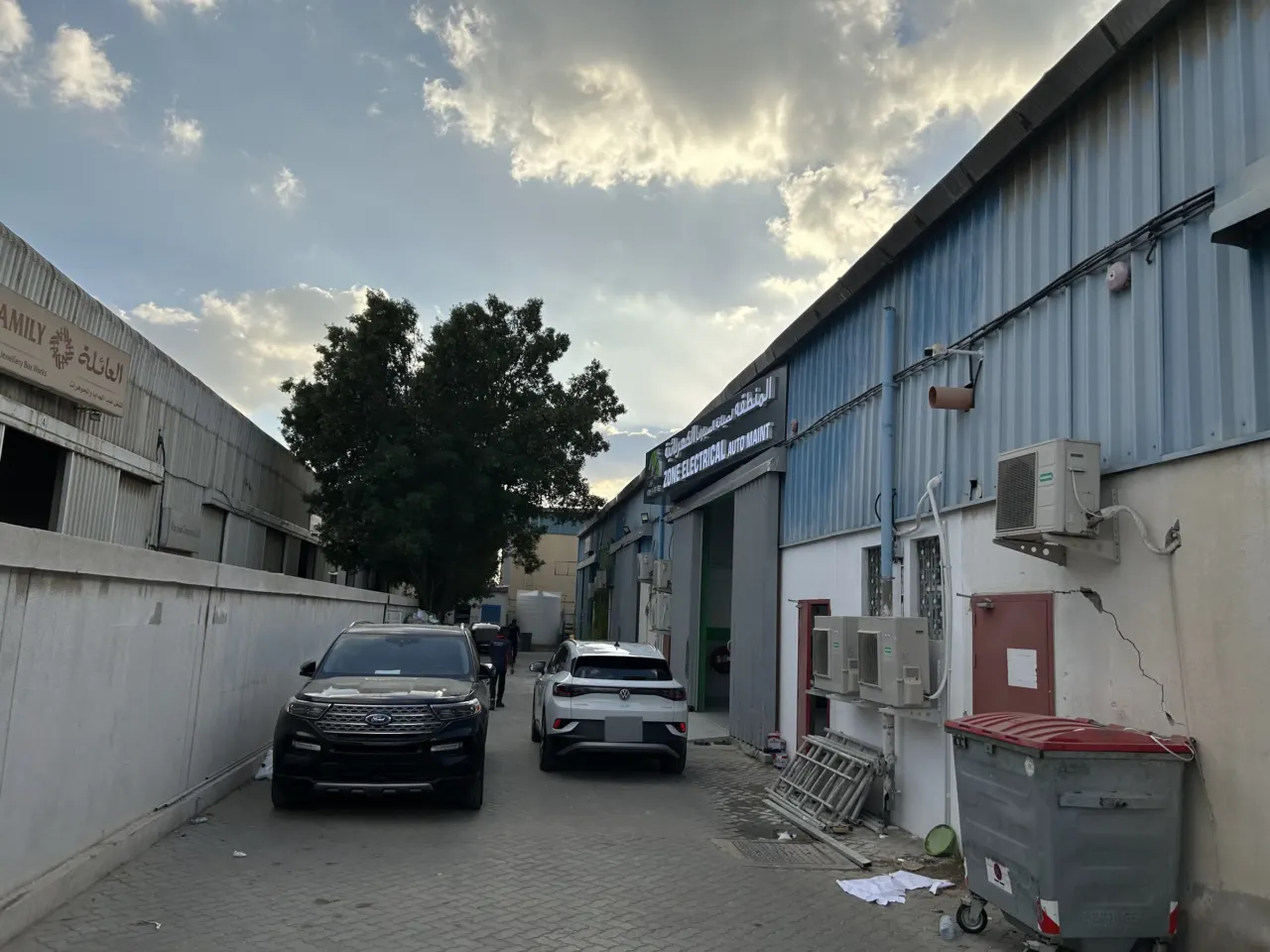 الطريق الفرعي المتفرع من شارع 18 في المنطقة الصناعية 11 بالشارقة، ولافتة EV Zone على المبنى الأيمن والسيارات متوقفة على جانب الطريق