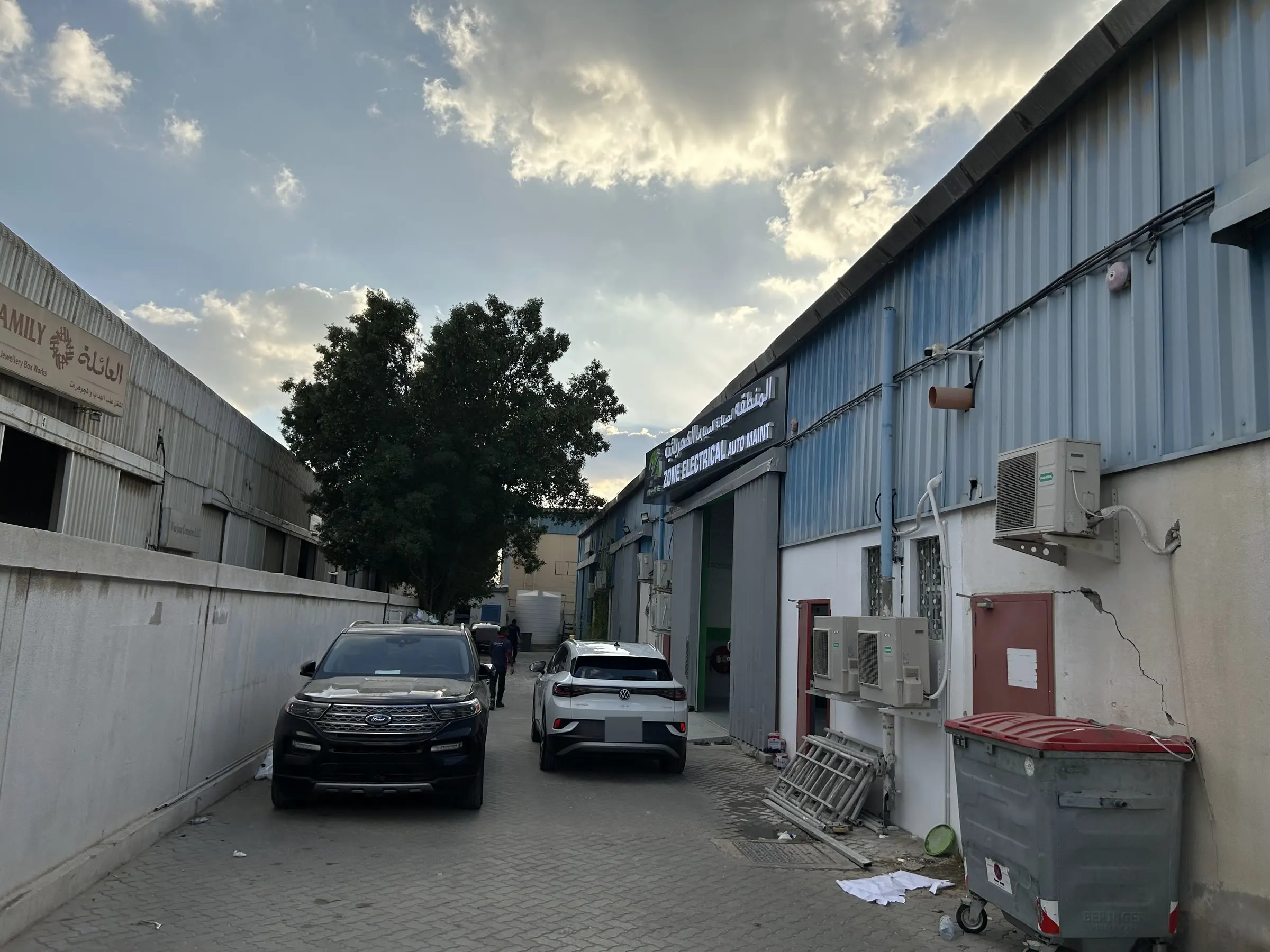 الطريق الفرعي المتفرع من شارع 18 في المنطقة الصناعية 11 بالشارقة، ولافتة EV Zone على المبنى الأيمن والسيارات متوقفة على جانب الطريق