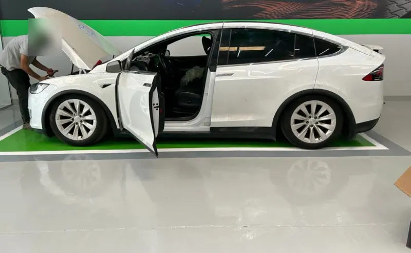 A white Tesla Model X with its front bonnet and driver's door open in a green-marked bay at EV Zone, with a technician working at the front