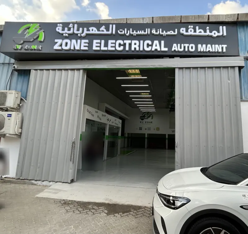 The EV Zone workshop entrance in Sharjah: the signboard with the Arabic trade name and ZONE ELECTRICAL AUTO MAINT above the open gate, with the bays inside