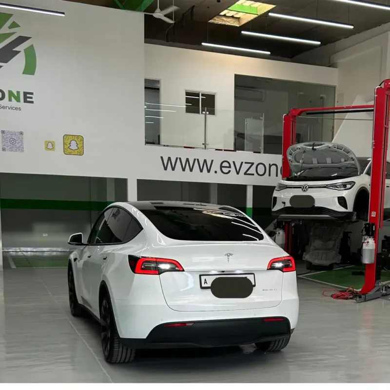 A white Tesla Model Y in the EV Zone workshop, with a Volkswagen ID.4 raised on a two-post lift behind it