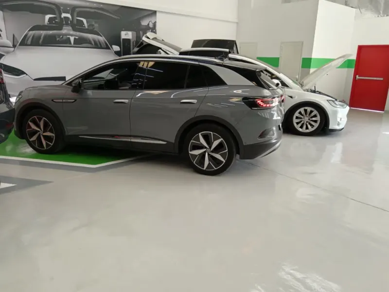 A grey Volkswagen ID.4 and a white Tesla Model X with its bonnet and rear door open, side by side in the EV Zone workshop bays