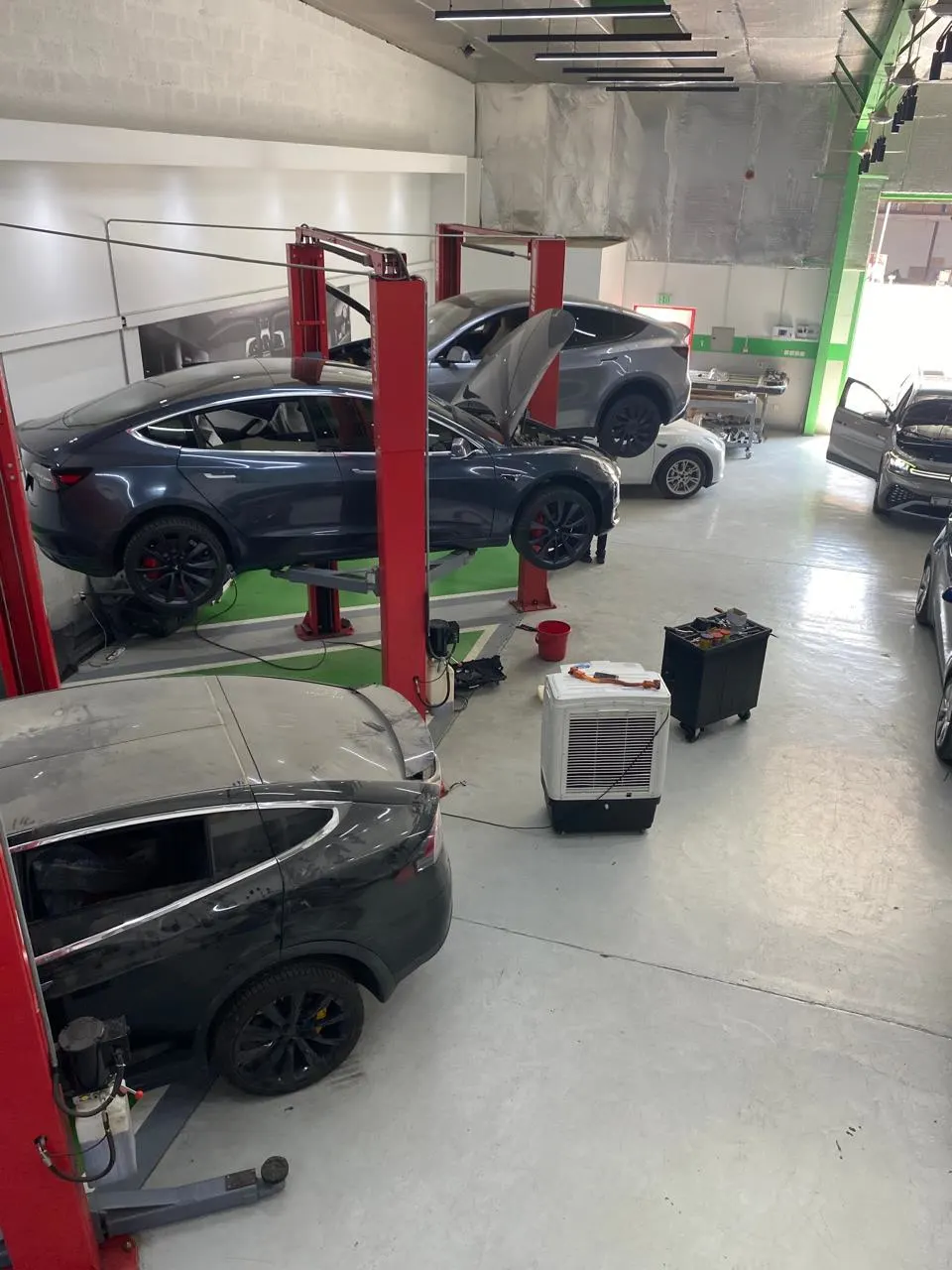 A Tesla Model 3 raised on a lift in the EV Zone workshop, with other EVs in the bays
